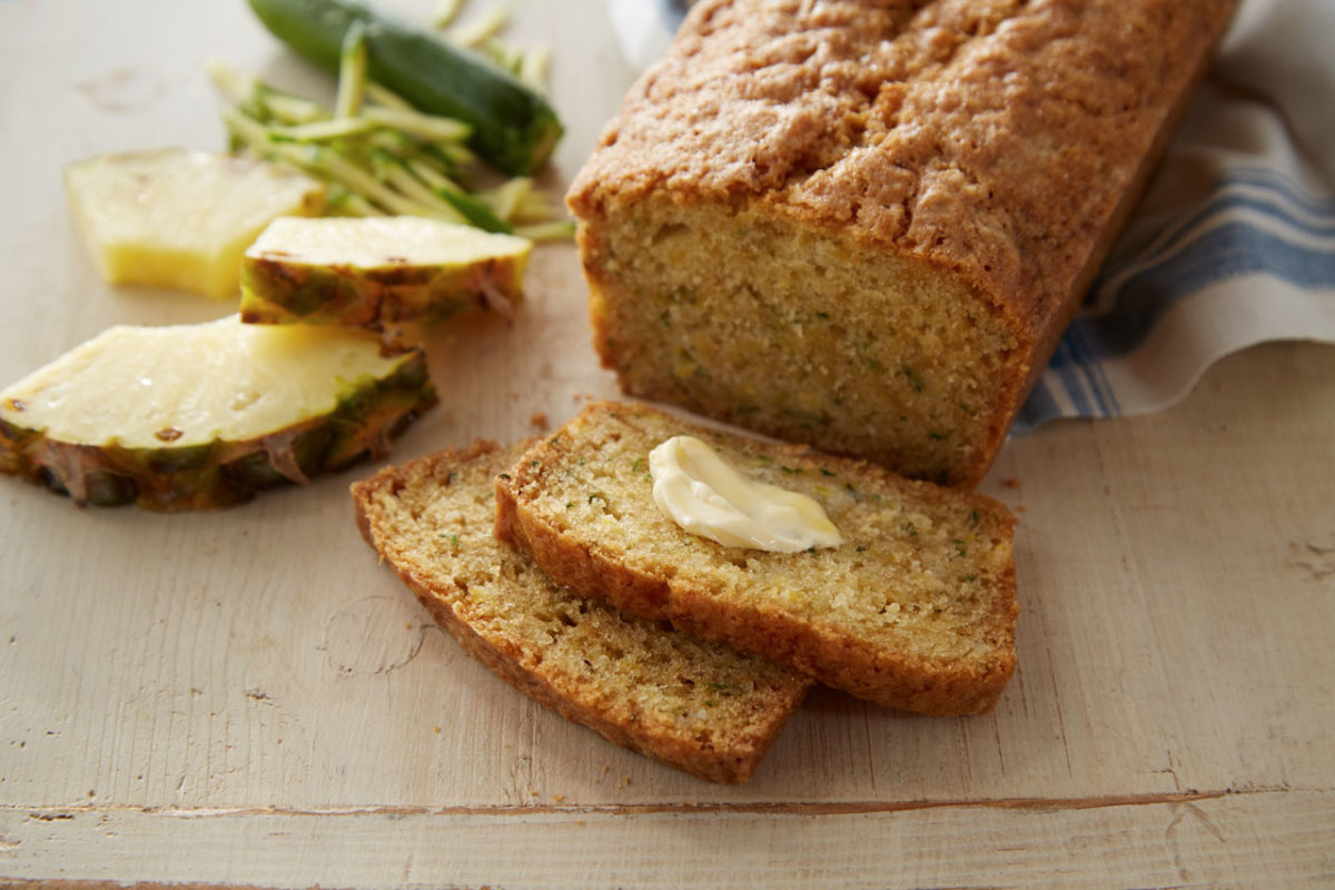 A slice of almond flour zucchini bread with butter on it and the rest of the loaf behind the slice